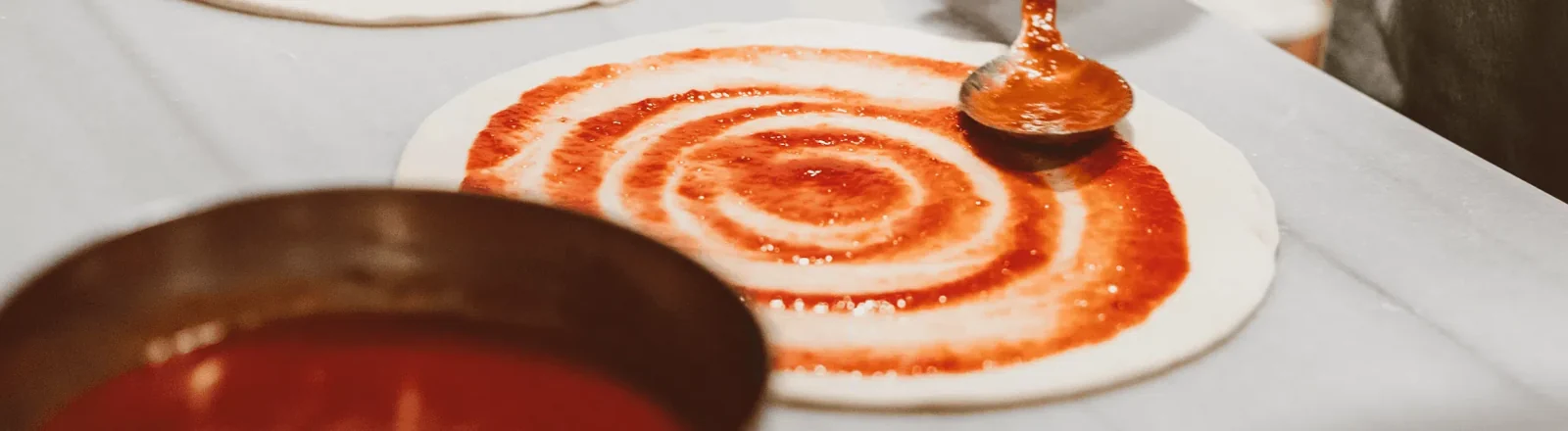 Sauce being spread on a pizza base, from the Vikmar Foods website